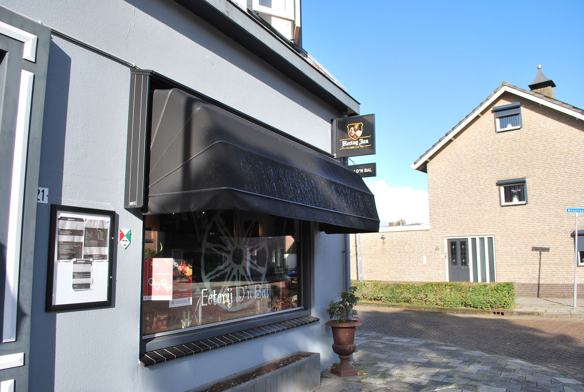Grijze winkelpui met zwarte luifel en uithangbord. Achter de winkelpui is een gebouw zichtbaar.