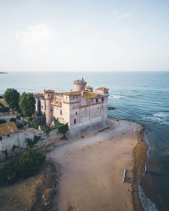 Roze kasteel op een zandstrand, met de oceaan rechts onder een heldere hemel.