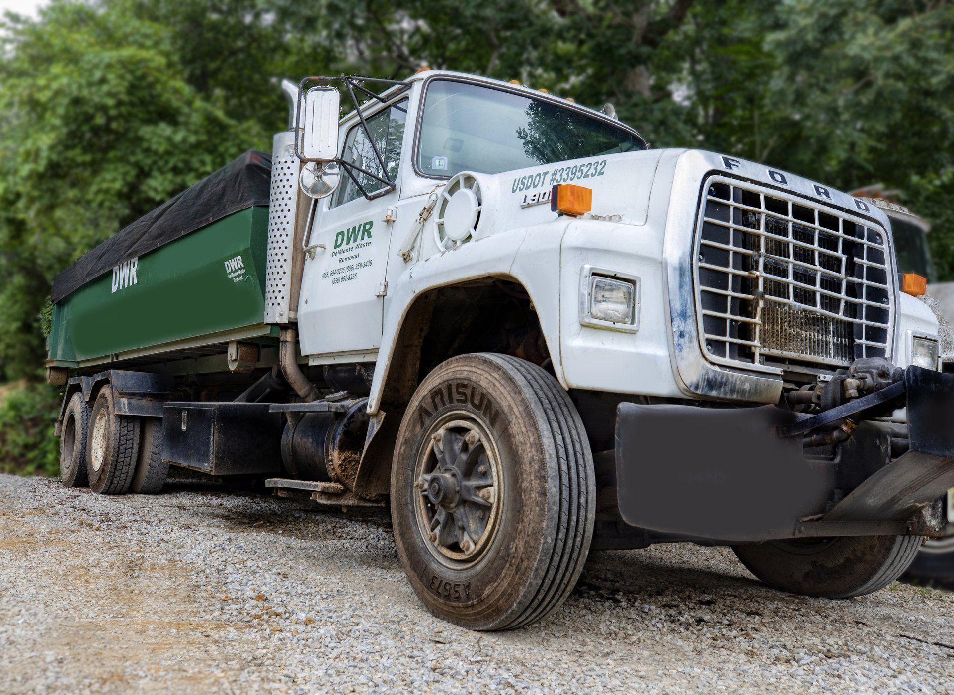 White Ford dump truck parked on gravel, with a green bed.