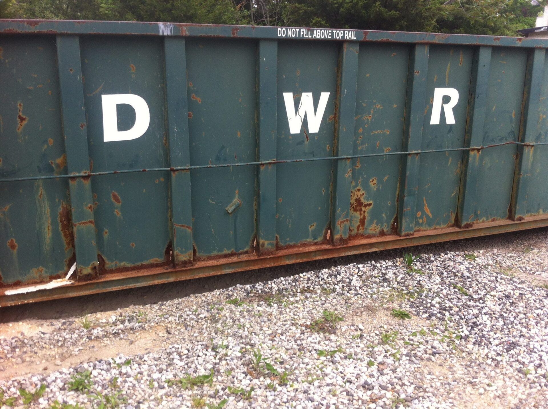 A large, blue metal roll-off dumpster sitting on a paved surface covered with patches of snow.