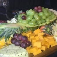 Fruit and cheese platter with green and purple grapes, mango cubes, and a wedge of soft cheese