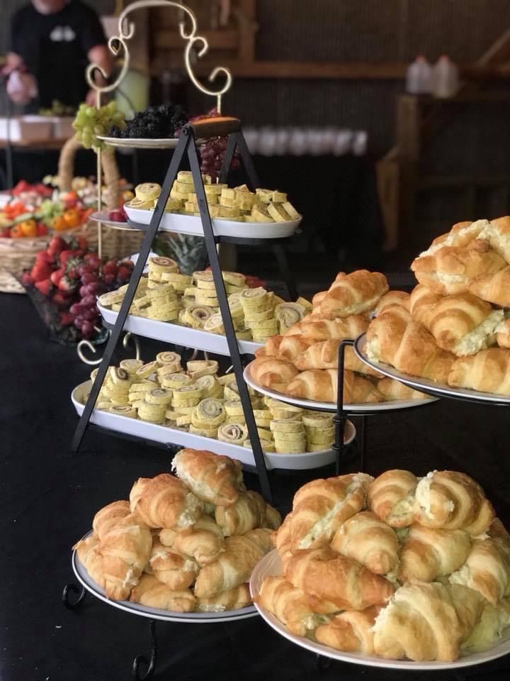 Tiered trays of croissants and pastries at a buffet table with fruit in the background