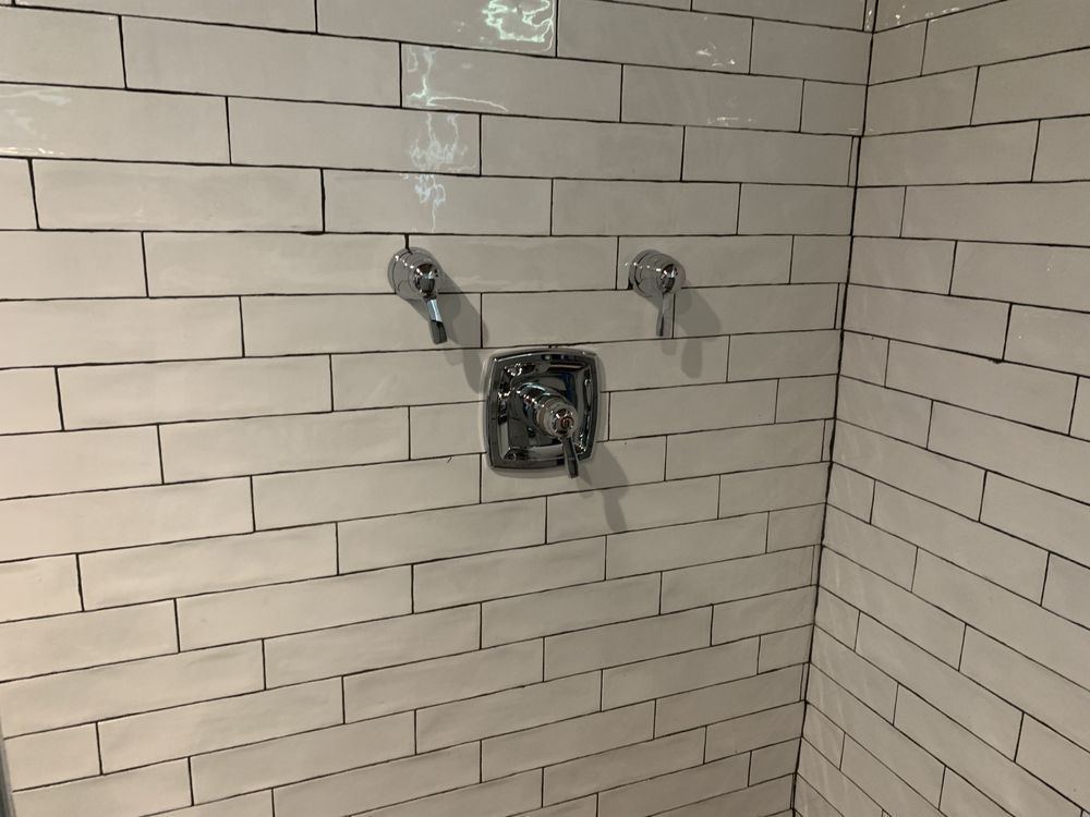 a shower with white tiles and chrome faucets
