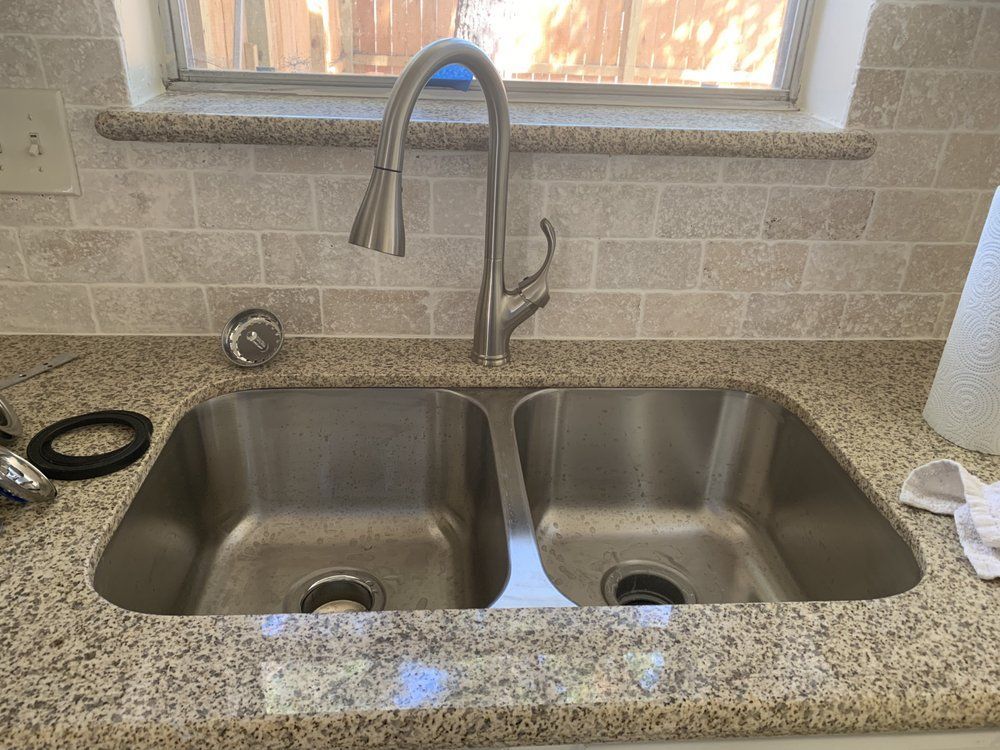 a stainless steel kitchen sink with a faucet on a granite counter top .