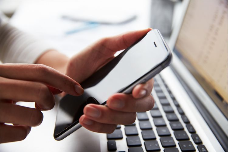 Hands holding a smartphone over a laptop keyboard, focusing on the screen interaction.