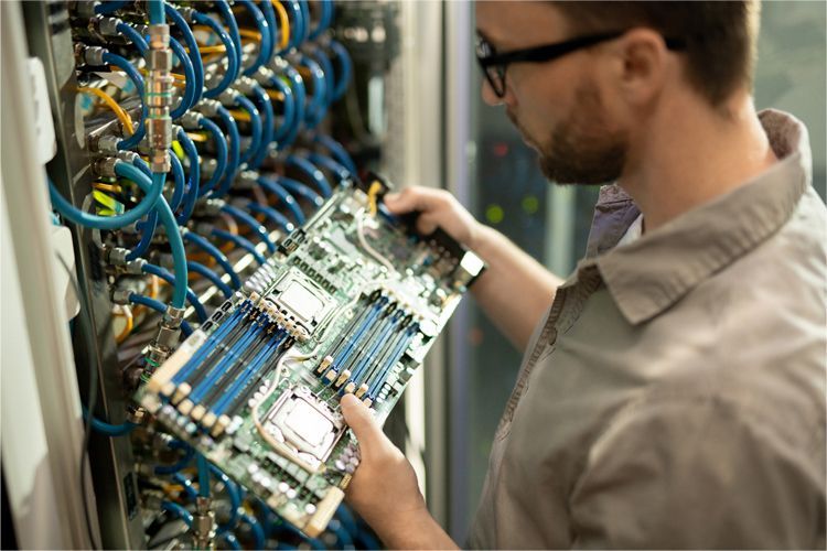 A person in a technical setting examining a server motherboard with blue memory modules and CPU sockets.