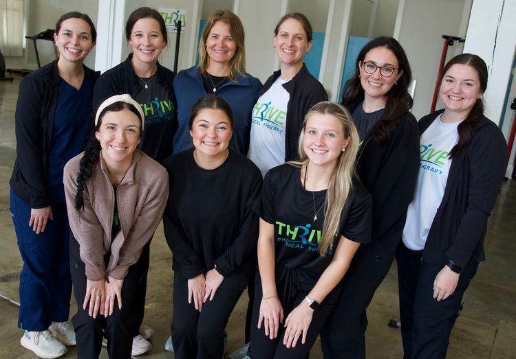 Eight women standing and smiling indoors in casual and business attire.