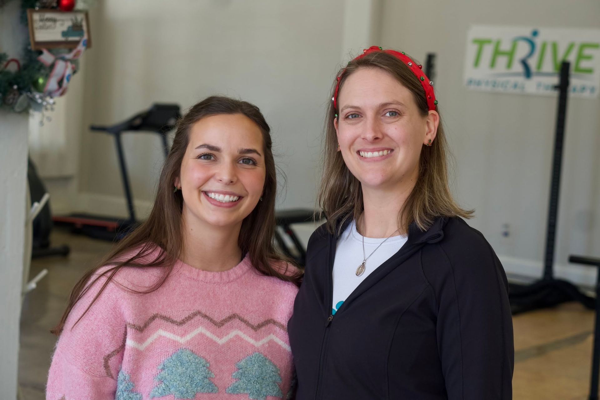 Two smiling women standing in a gym, with exercise equipment and a THRIVE sign in the background