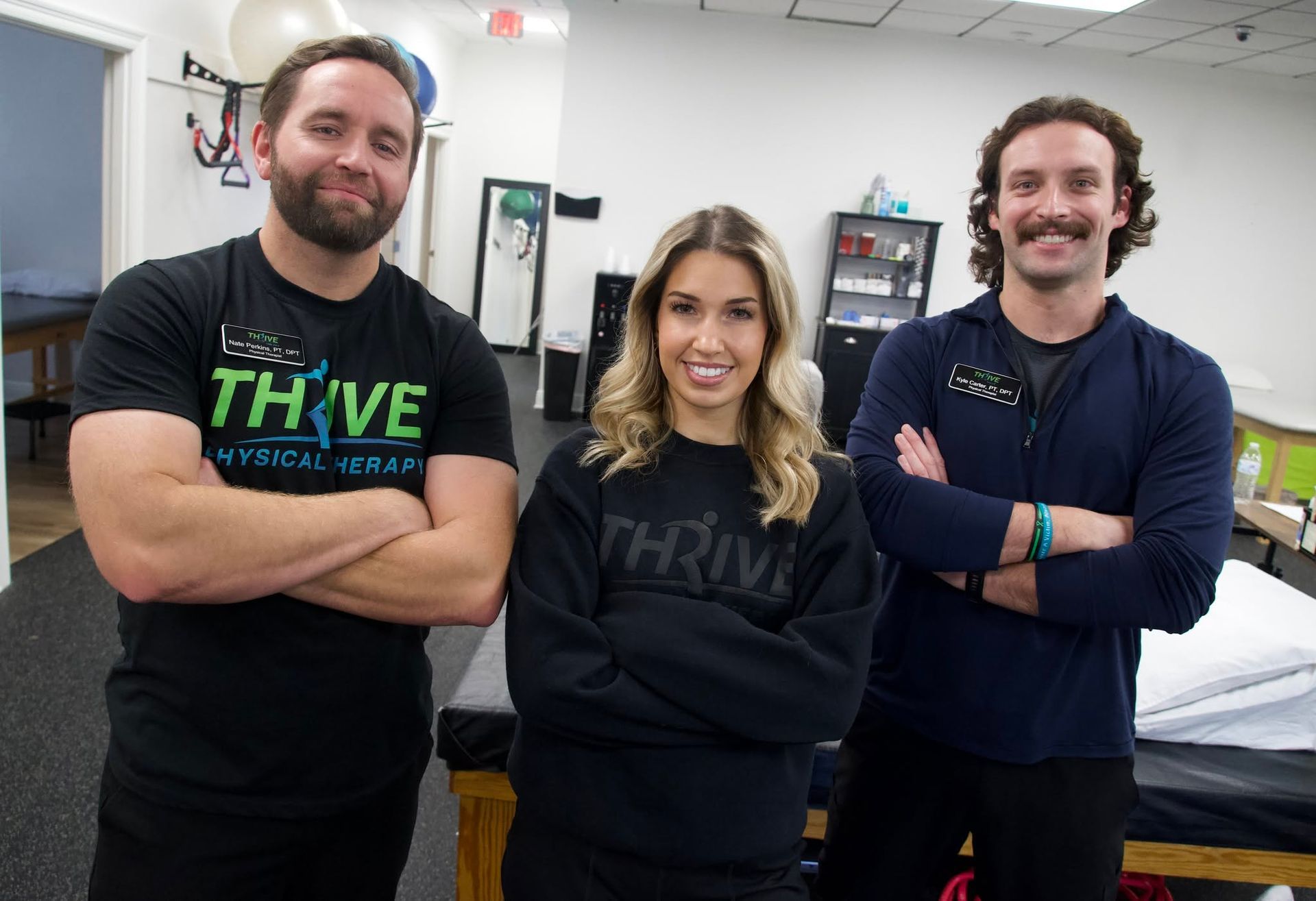 Three people in black Thrive shirts stand smiling with arms crossed in an office.