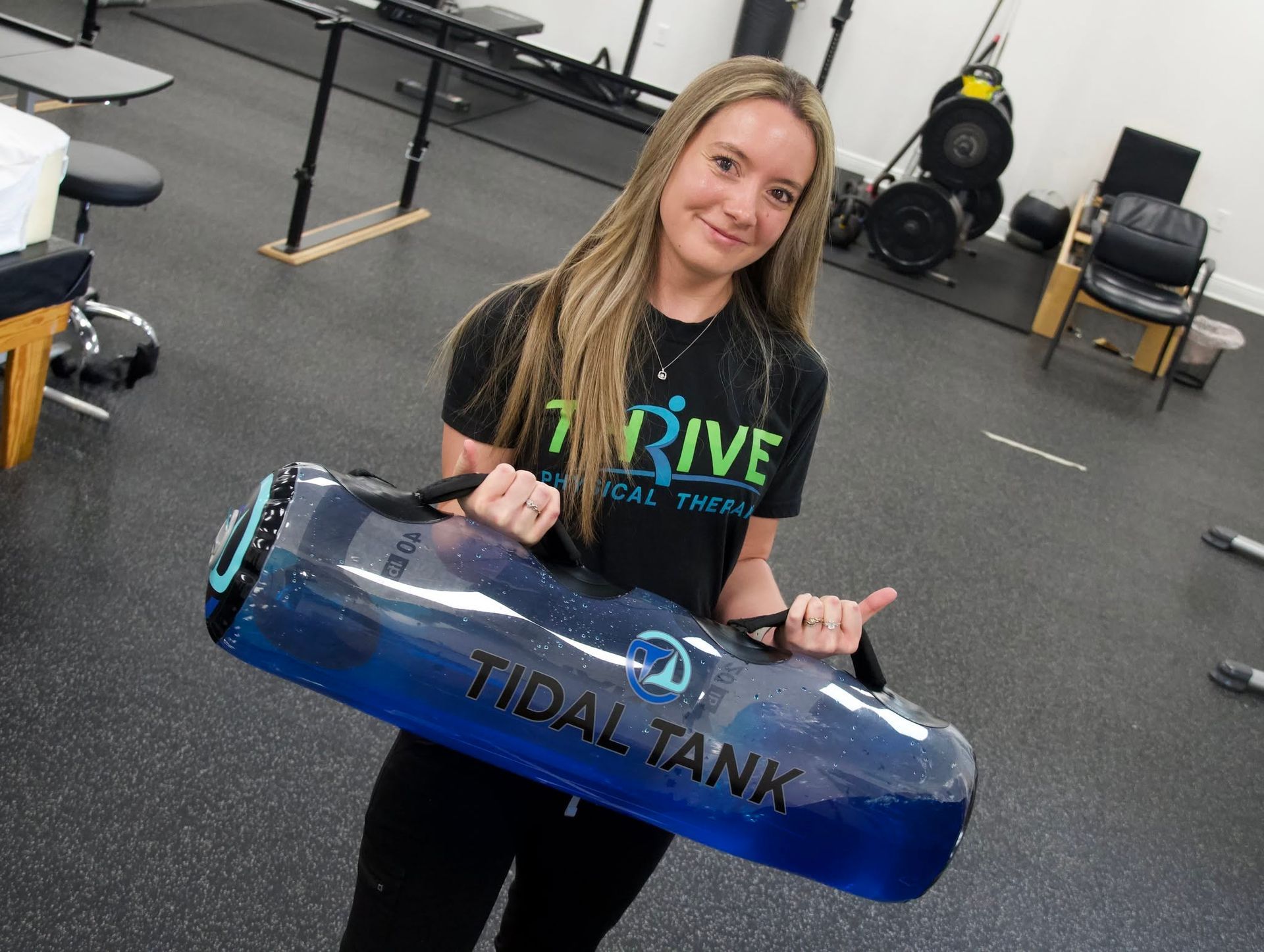 Woman holding a blue-and-black tidal tank in a gym or training space