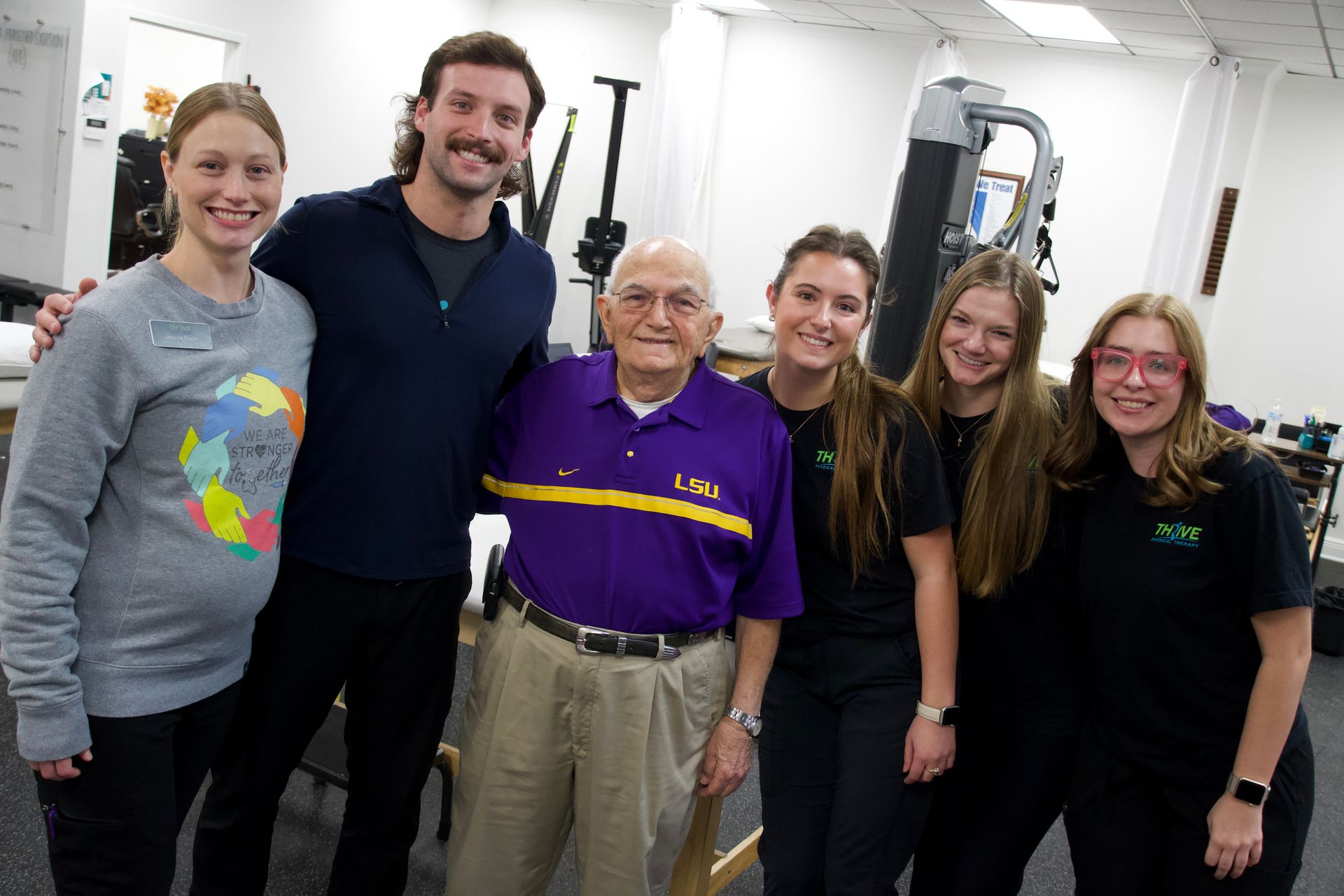Five people smiling in a gym, standing together in front of exercise equipment.