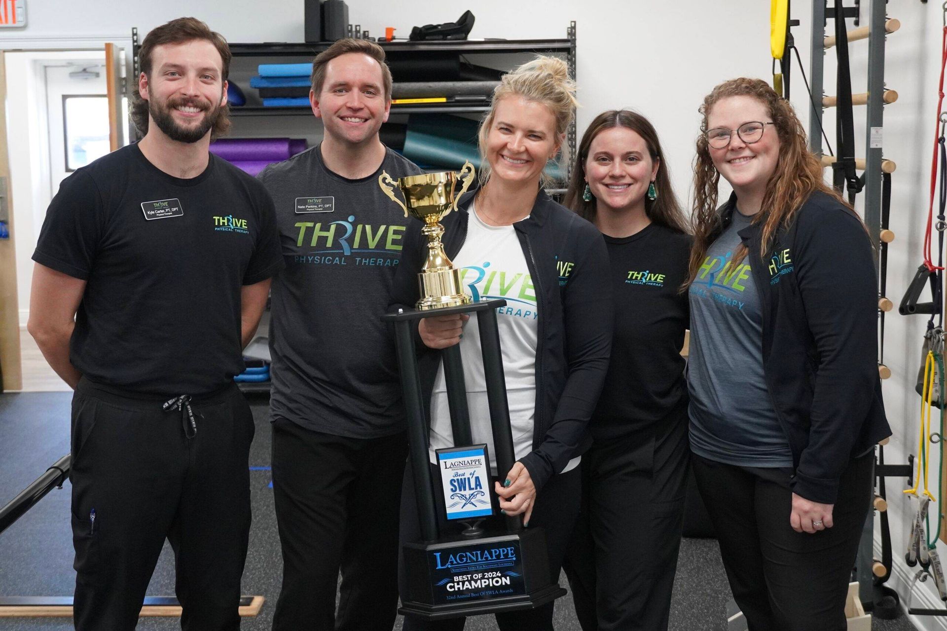 Five people smiling indoors, standing around a trophy and award plaque in a workshop or garage.