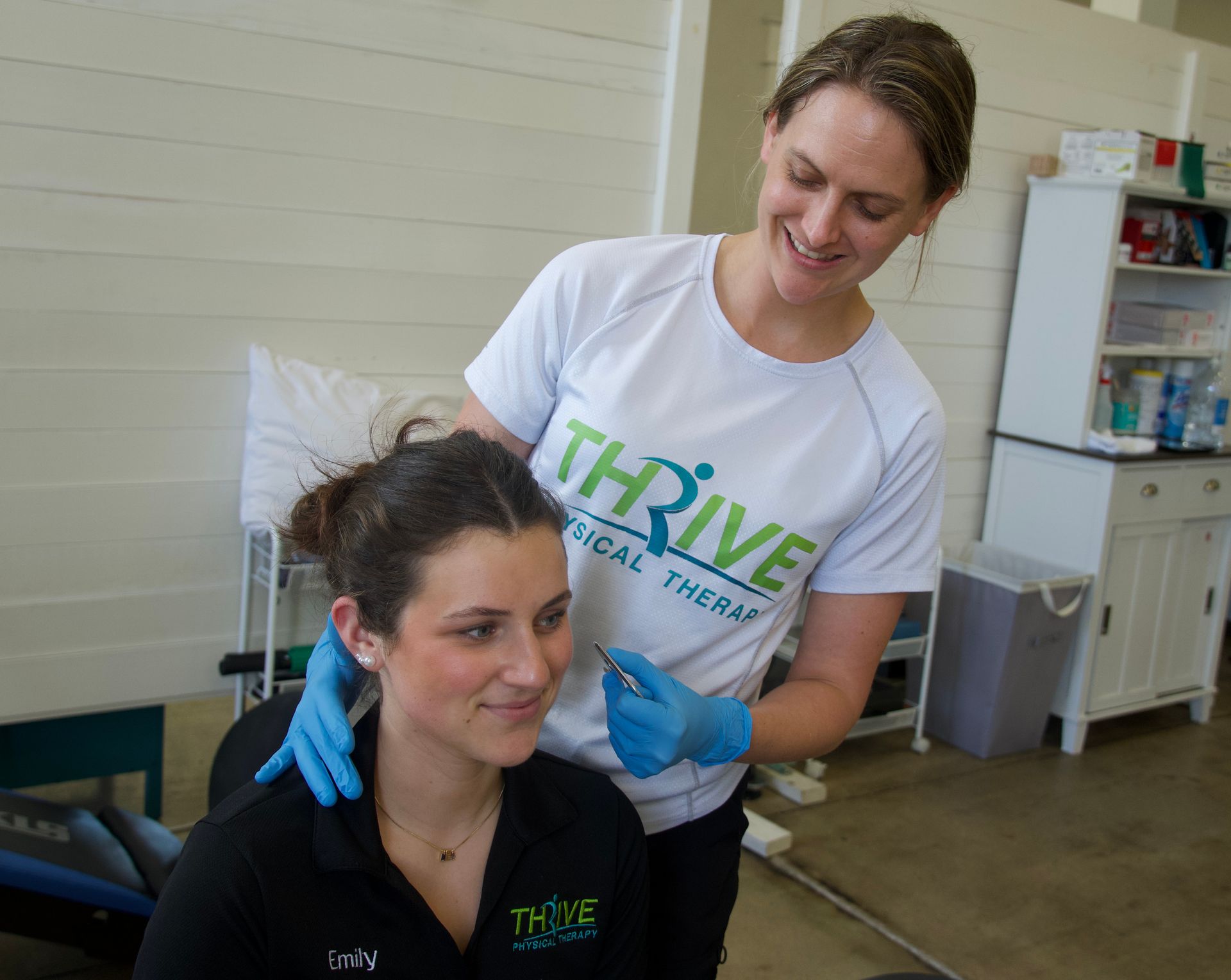 Therapist applying treatment to a seated woman in a clinic, both wearing blue gloves