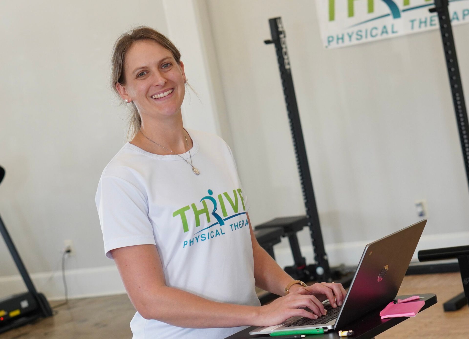 Woman smiling while typing on a laptop in a physical therapy clinic.