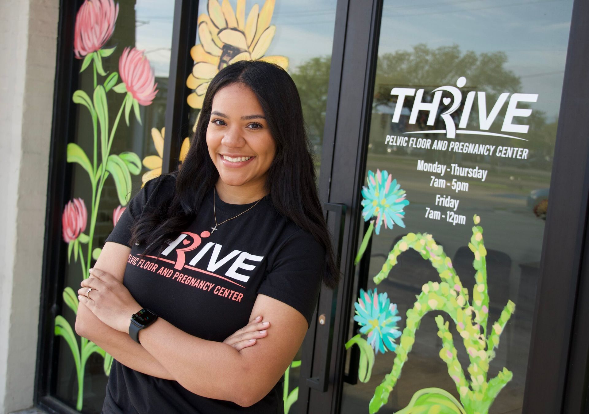 Woman smiling with arms crossed in front of THRIVE counseling office window with colorful flower art