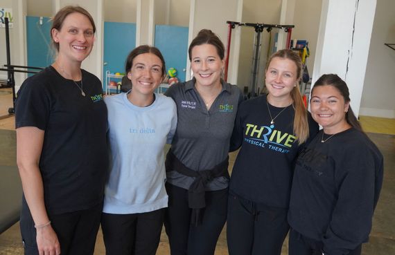 Five smiling people standing together indoors in a gym or studio setting
