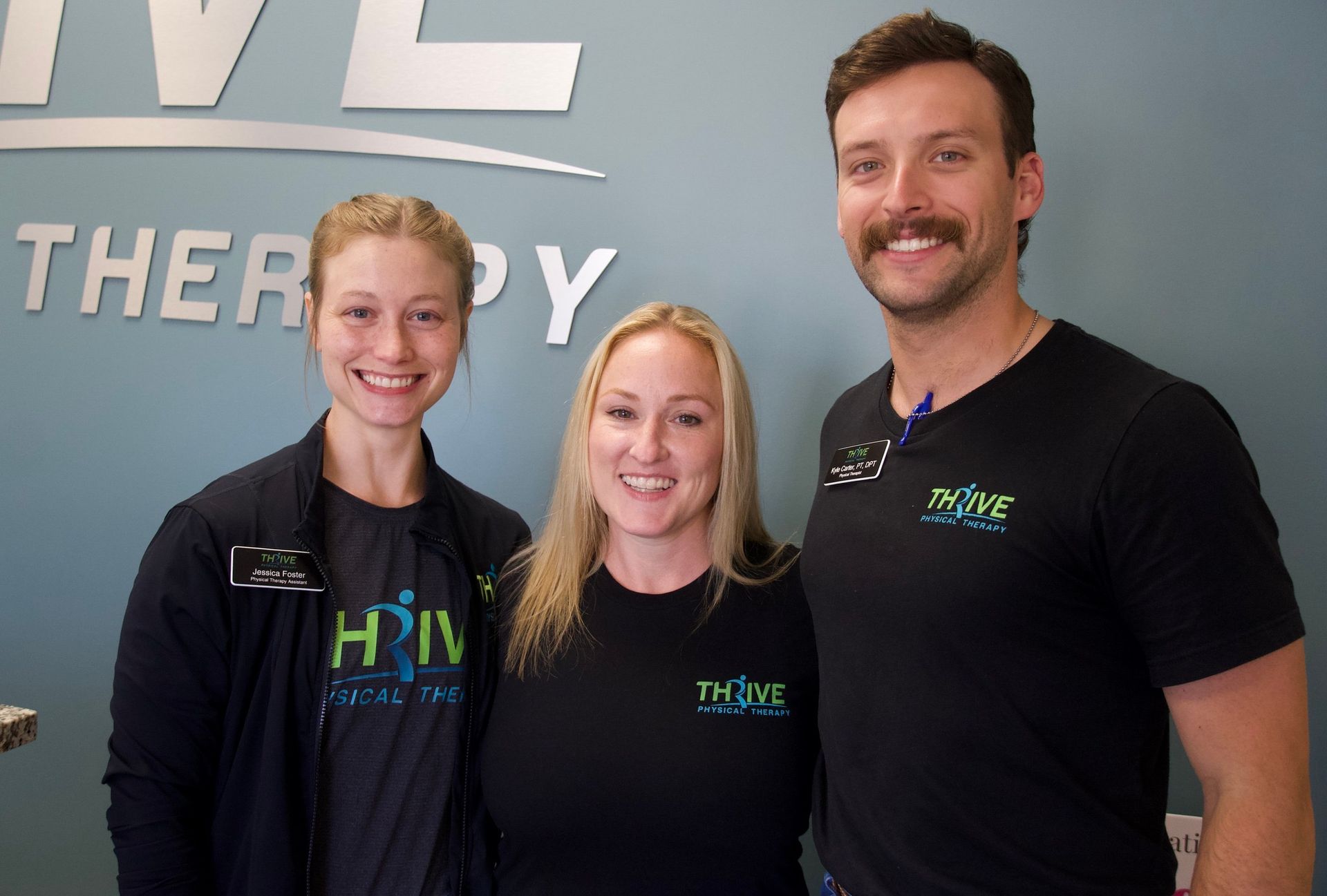 Three smiling staff members standing in front of a therapy clinic wall sign