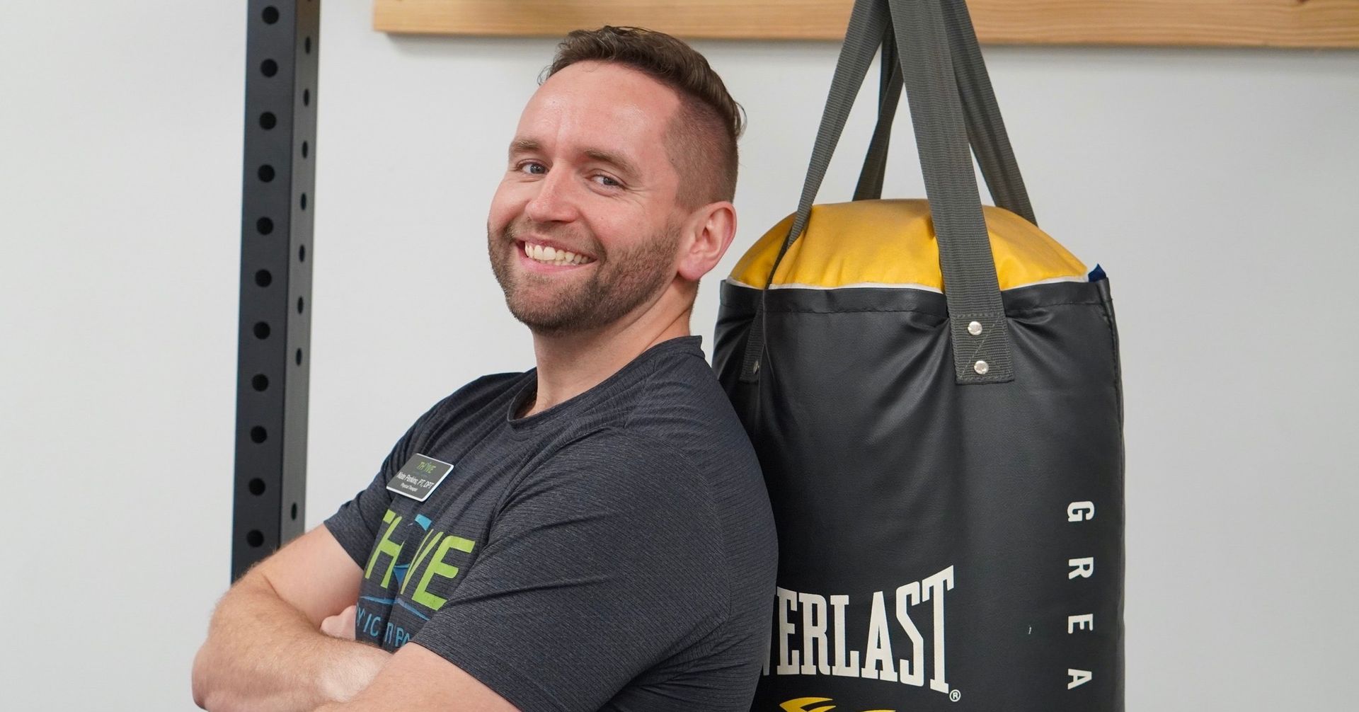 Smiling man with folded arms beside a black-and-yellow punching bag in a gym