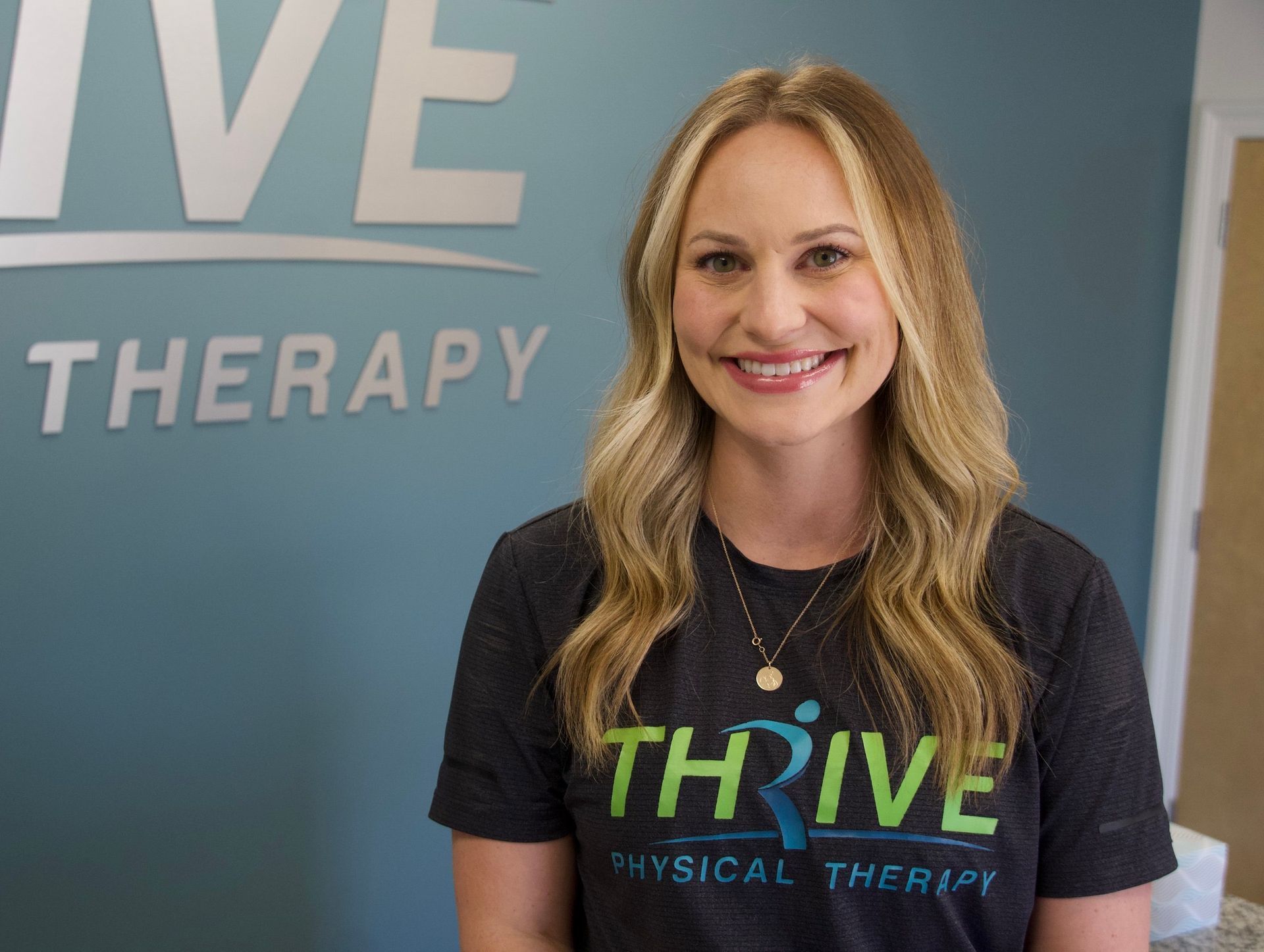 Woman smiling in a Thrive Therapy office, wearing a black Thrive shirt.