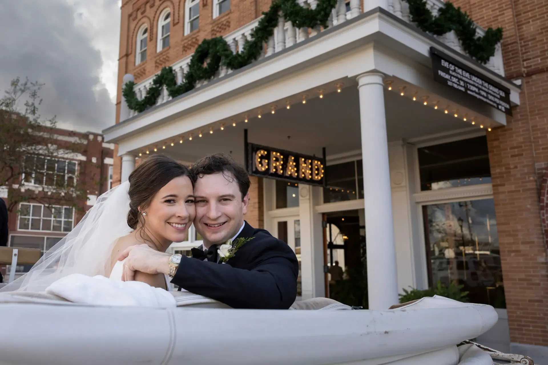 Smiling bride and groom in a white carriage outside a decorated brick building in winter