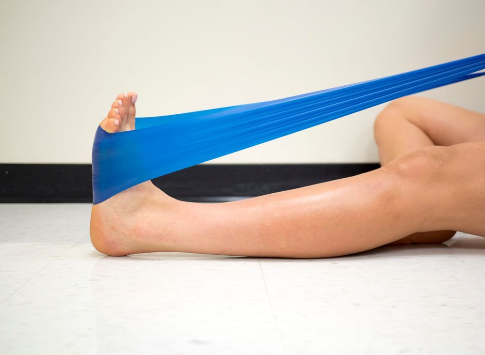 Person stretching foot with a blue resistance band while lying on the floor