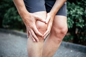 Hands holding an aching knee outdoors on a path