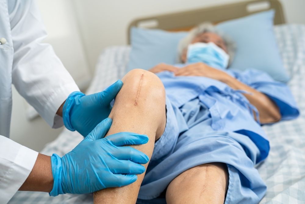 Medical professional examining a patient’s knee in a hospital bed