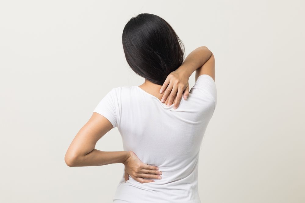 Person in white shirt holding neck and lower back, suggesting pain or discomfort