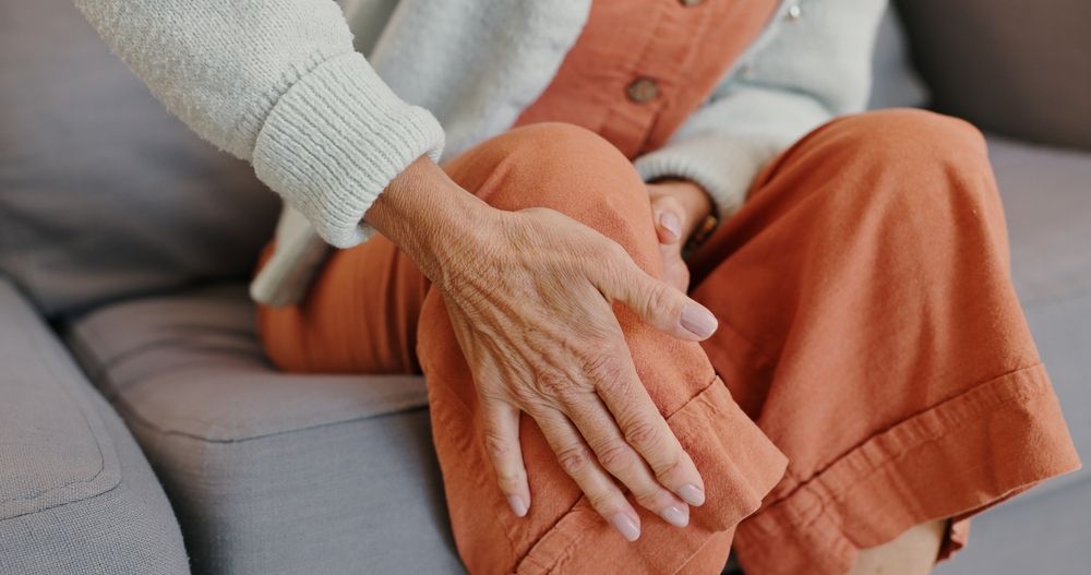Hands resting on a seated person’s orange pants beside a gray sofa