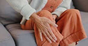 Hands gently resting on a person’s orange-clad knee while seated on a gray sofa