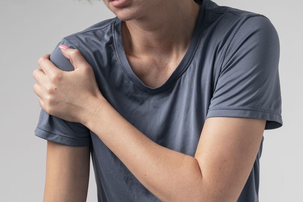 Person in a gray shirt clutching their shoulder, indicating pain or injury.