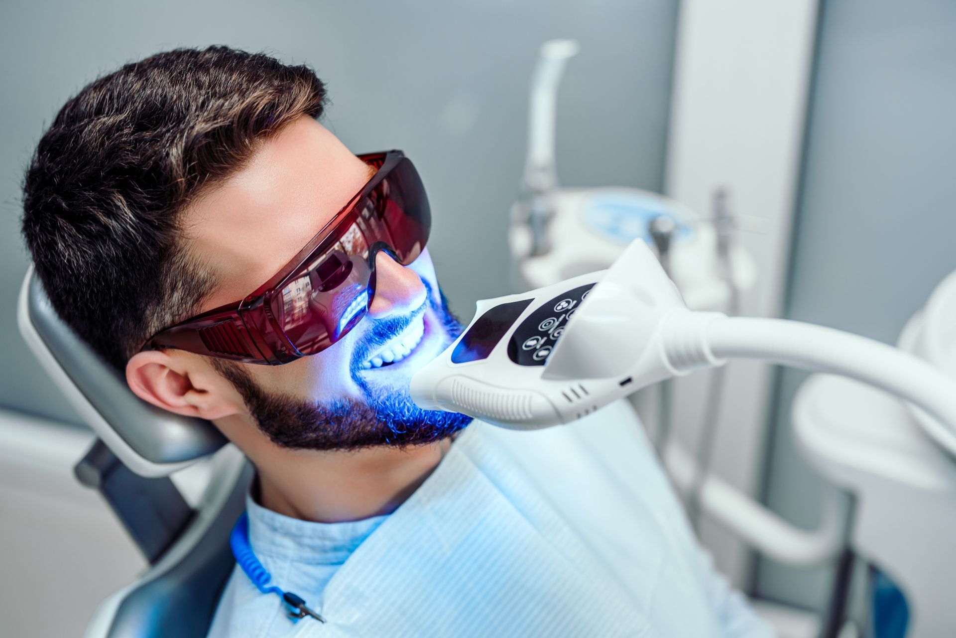 A patient wearing protective glasses is undergoing a teeth whitening procedure.