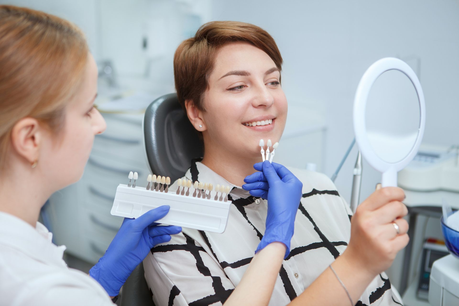 Dentist showing teeth shades to a woman patient, comparing with a mirror, in a dental clinic. Dentist showing teeth shades to a woman patient, comparing with a mirror, in a dental clinic.