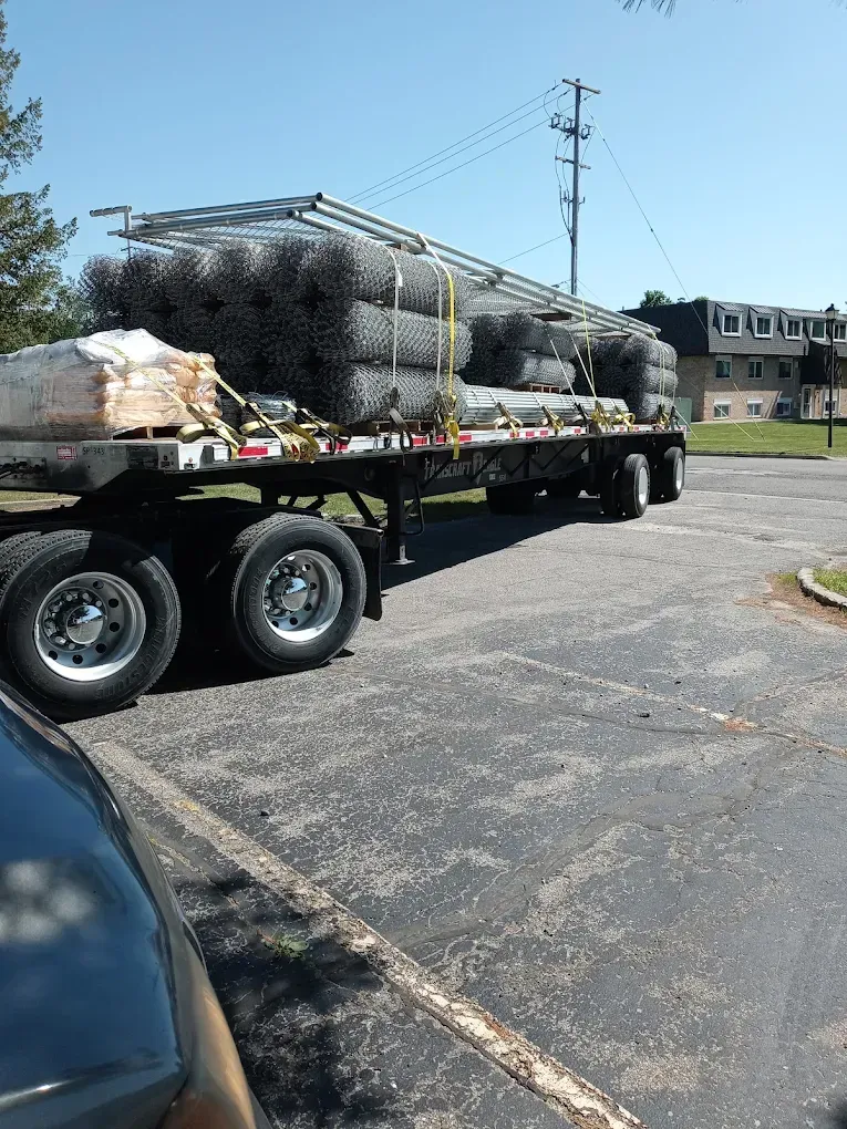 Flatbed truck loaded with wrapped cargo parked in a lot near a utility pole and buildings.