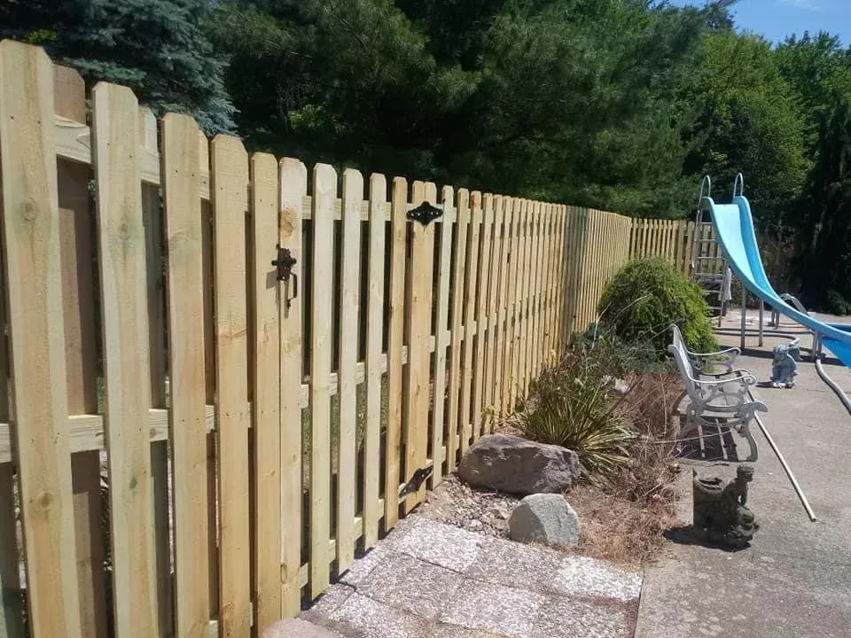 Wooden fence beside a backyard patio with planters and a blue slide in the background