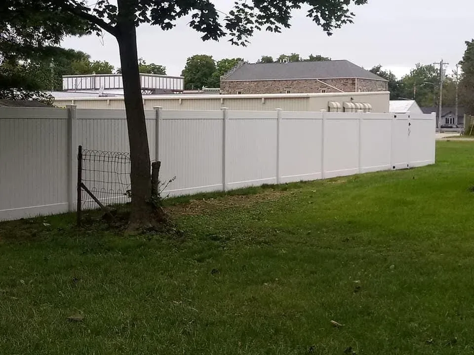 White vinyl fence beside a grassy yard with a tree and cloudy sky