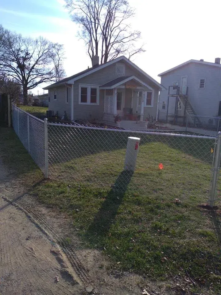 Small house with a chain-link fence and grassy front yard on a sunny day.