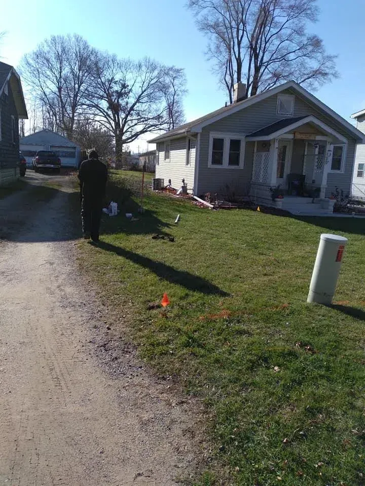 Person standing on a sunny residential street beside a small white house and grassy yard