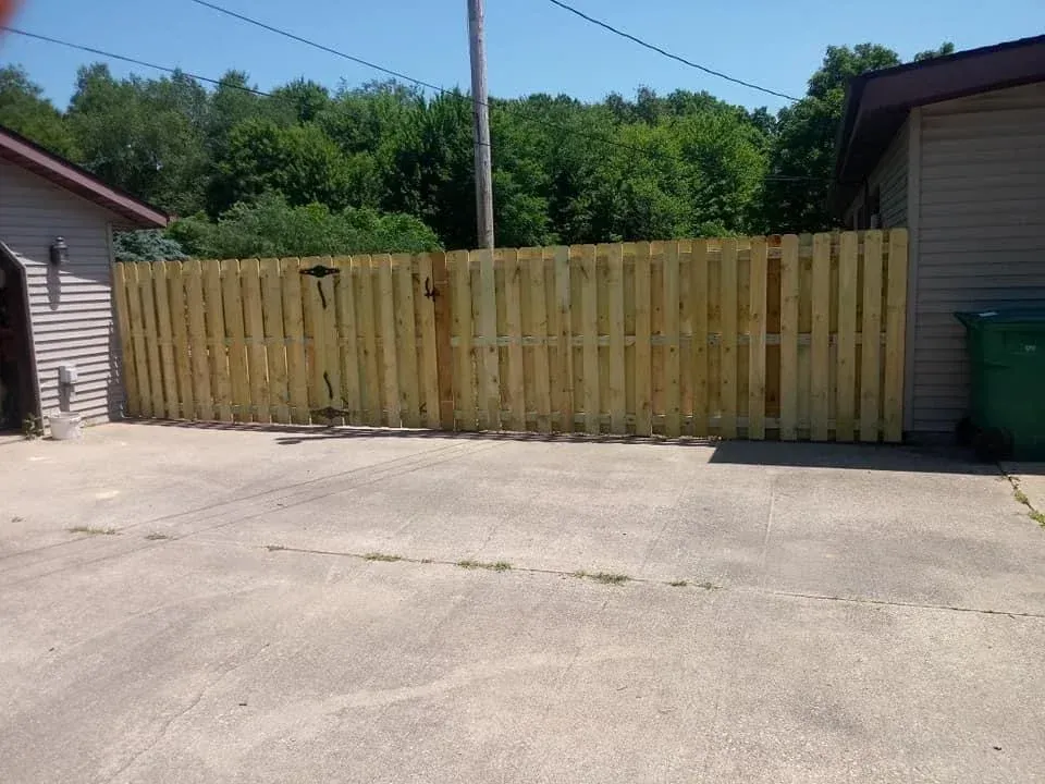 Driveway blocked by a wooden privacy fence between two buildings under a blue sky
