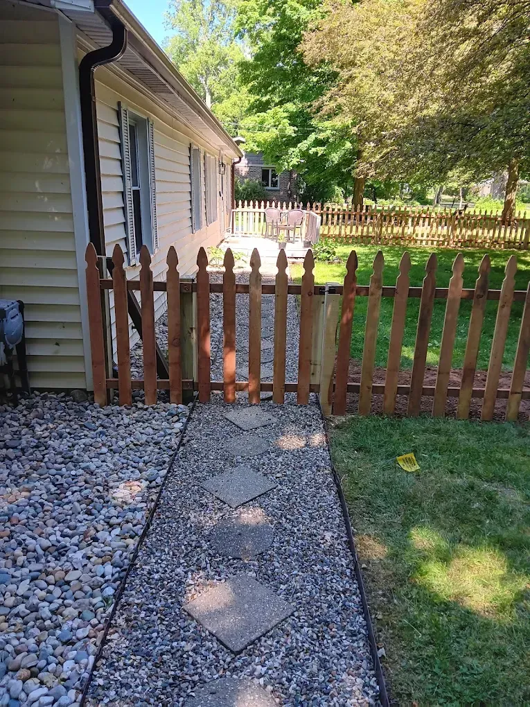 Gravel path leading to a wooden gate beside a house, with a fenced backyard beyond.