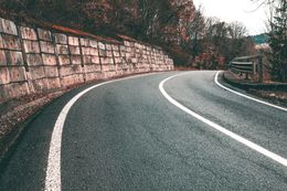 Curving empty road beside a stone retaining wall in a wooded area