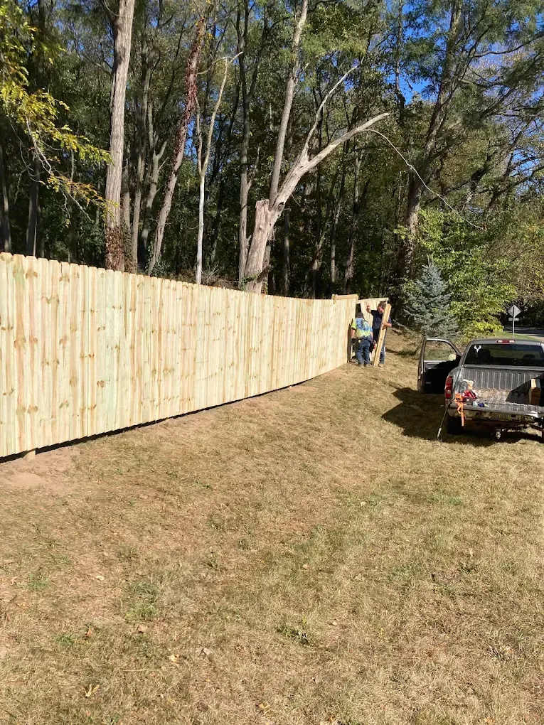Wooden fence along a grassy yard with trees, and a parked car near the fence.