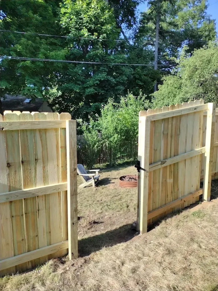 Open wooden gate leading to a backyard with trees and a dirt path