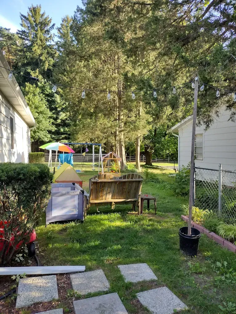 Backyard garden between two houses with trees, stepping stones, a bench, and a small play area in the distance