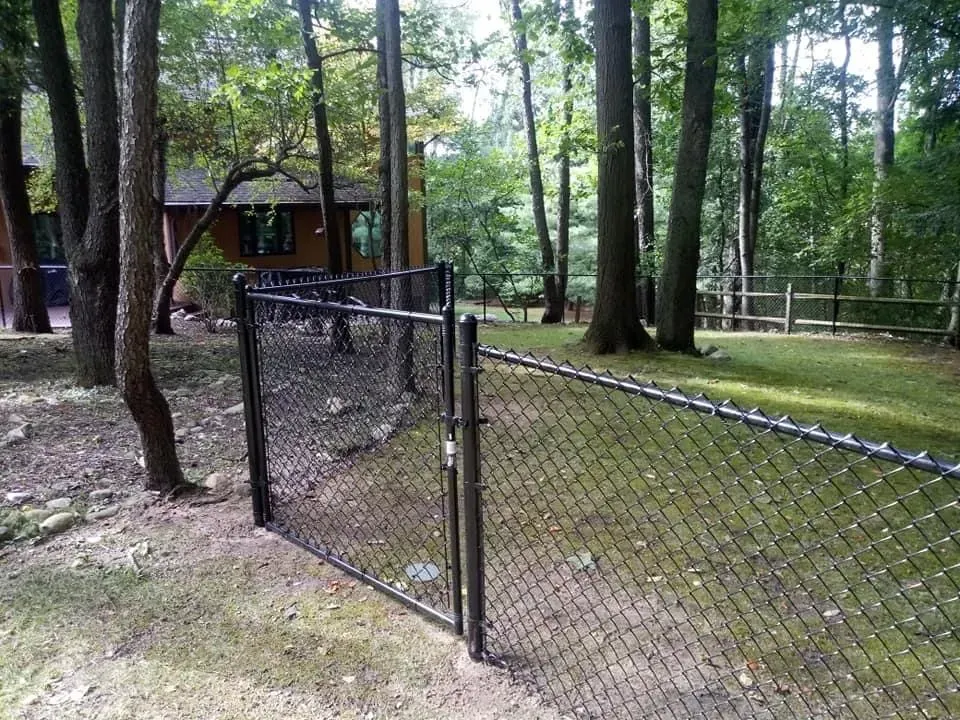 Chain-link fence along a wooded park path beside a small pavilion and cabin