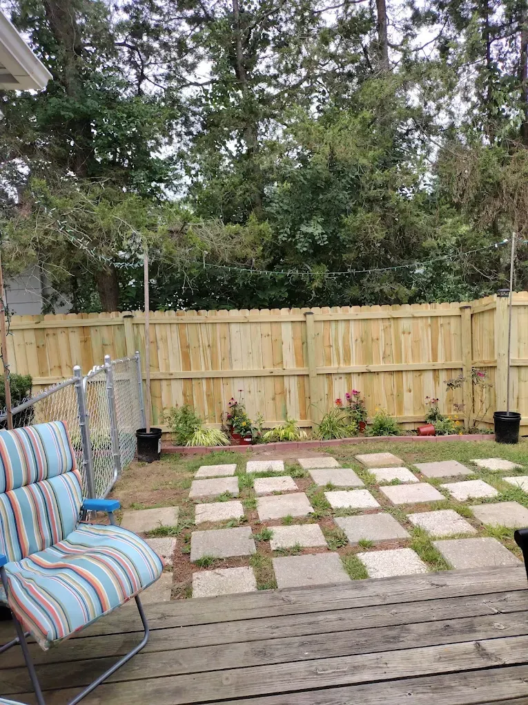 Backyard patio with striped chair, wooden deck, square paver path, and fenced garden area