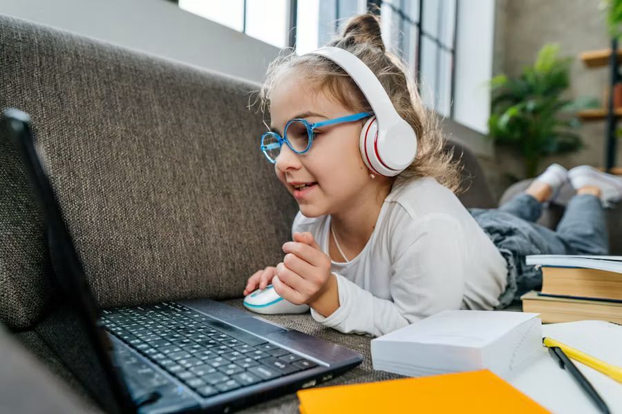Child busy on laptop with books next to her