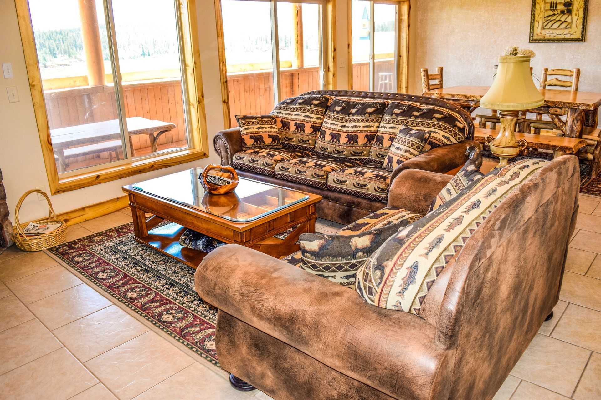 Cozy living room with brown leather sofa and patterned loveseat, coffee table on patterned rug, with large windows.