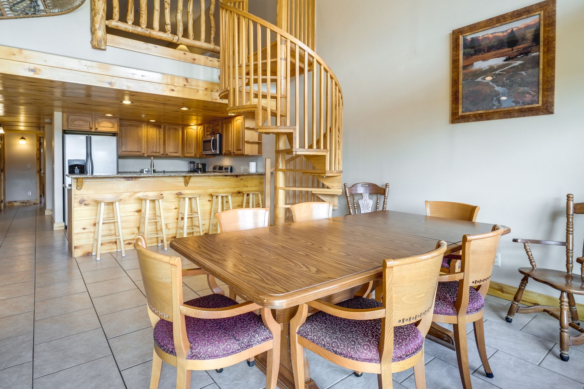 Dining room with a spiral staircase, kitchen, and six chairs around a large table. Bright, wood tones throughout.