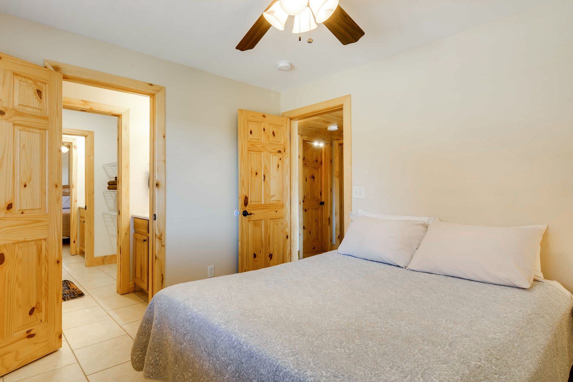 Bedroom with a bed, wooden doors, and a ceiling fan. One door leads to a hallway with a bathroom.